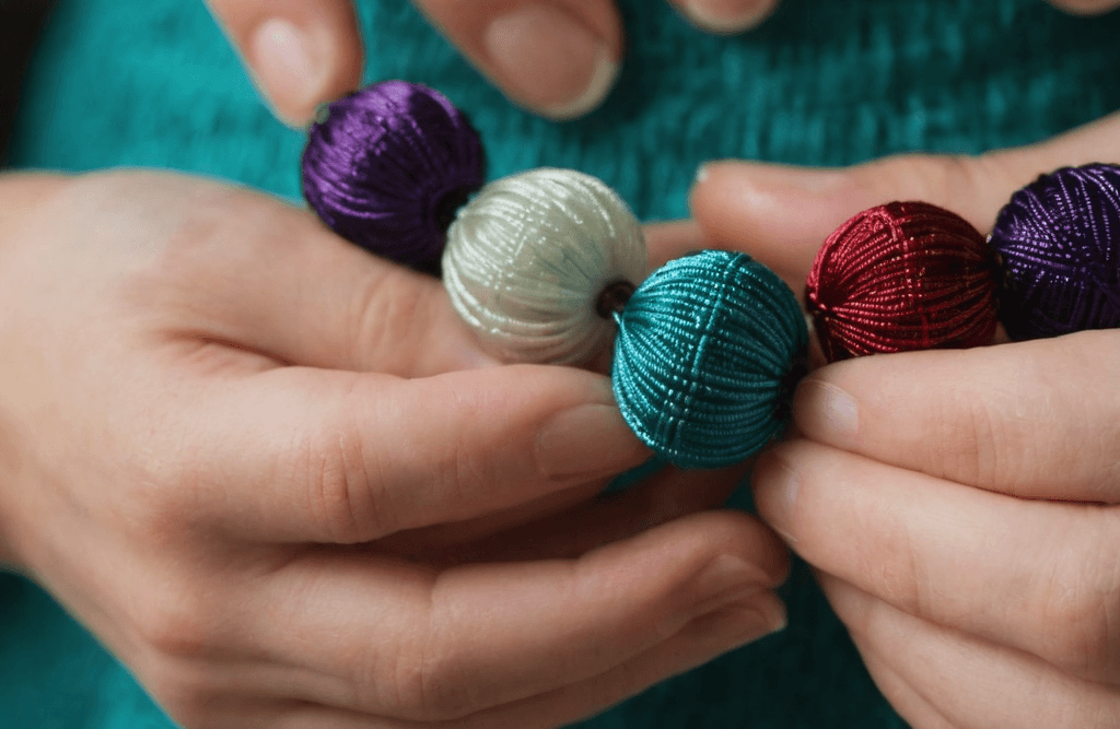 A close-up shot of hands carefully crafting a beaded necklace using natural materials like colorful beads and silk thread.